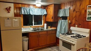 A compact kitchen with wooden cabinets, a refrigerator, a stove, and a sink.