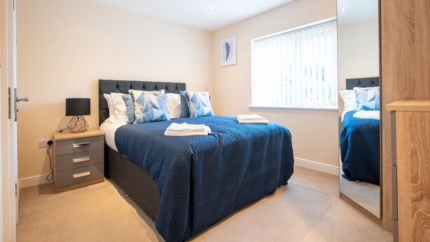 A bedroom with a large bed, bedside tables, a mirror, and a window with blinds. - Apartment 9 (Worksop)