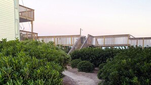 Un sentier en bois mène à une terrasse en bois agrémentée d’une rambarde, le tout étant entouré d’une végétation luxuriante.
