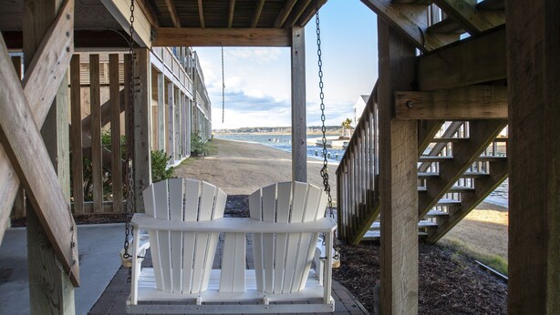 Une terrasse en bois avec un fauteuil suspendu donnant sur une plage.