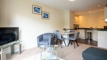 A modern living room with a glass coffee table, a sofa, a TV, and a dining area with chairs and a table.