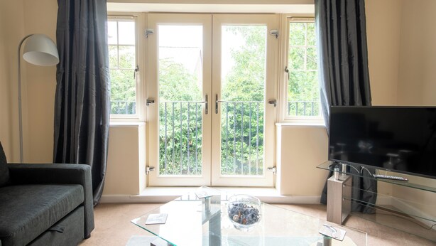 A living room with a sofa, a glass coffee table, a TV on a stand, and a balcony with curtains. - No16 (Mansfield)