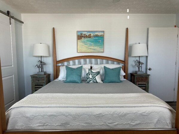 Un dormitorio con una cama, dos mesitas de noche, un tocador, un cuadro y una puerta.