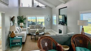 Uma sala de estar ampla com pé direito alto, grandes janelas, lareira e televisão.
