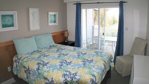 Une chambre à coucher comprenant un lit, une table de chevet, une chaise et un balcon avec vue sur les arbres.