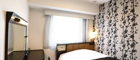 Quarto de hotel com cama, secretária, espelho e janela com cortinas.