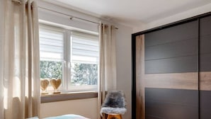 Een slaapkamer met een bed, een stoel, een raam met gordijnen en een schuifdeur.