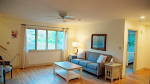 Uma sala de estar com sofá, mesa de centro, luminária e ventilador de teto.