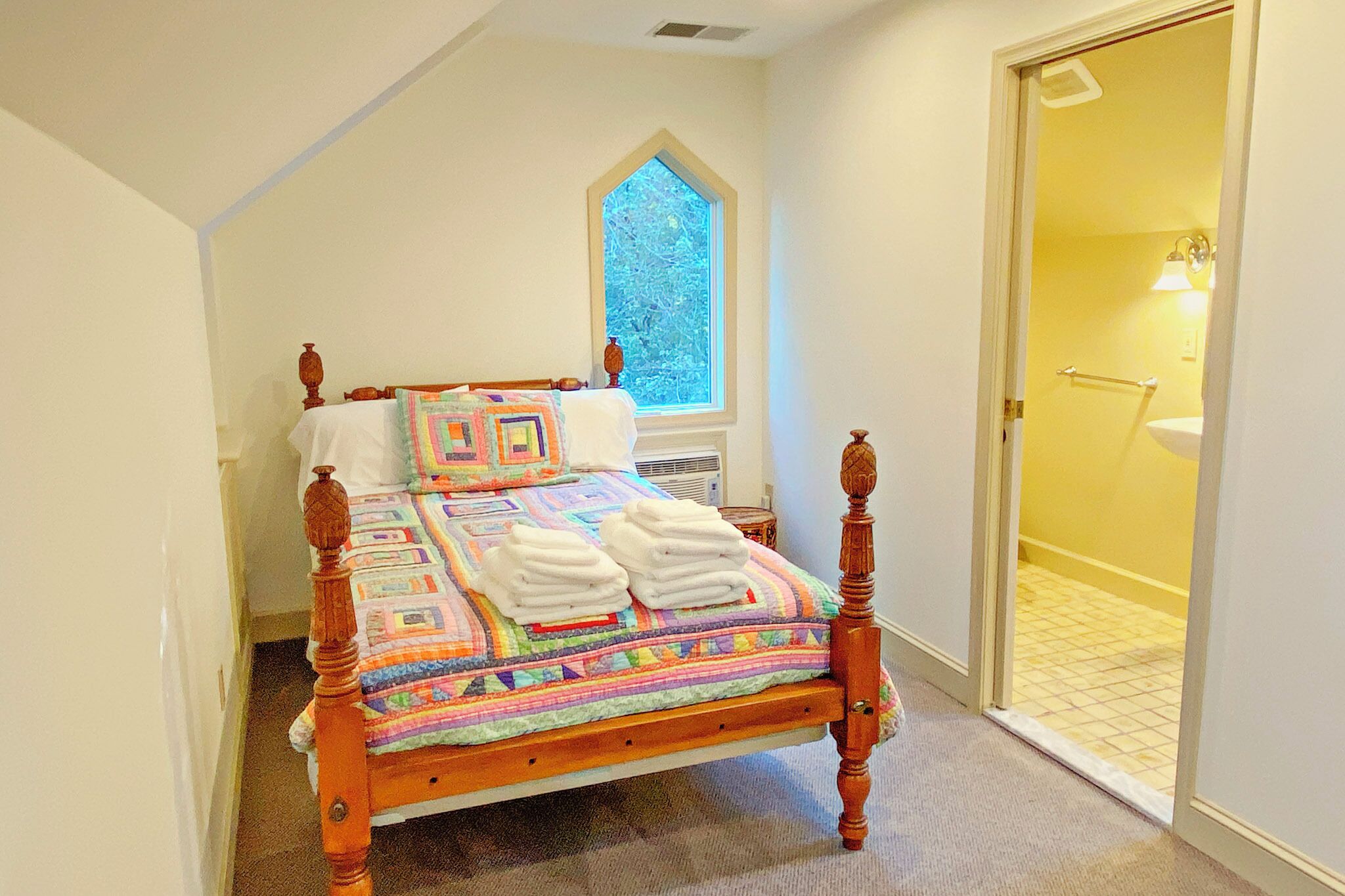 Un dormitorio con cama de madera, colcha colorida y ventana con vistas a árboles.