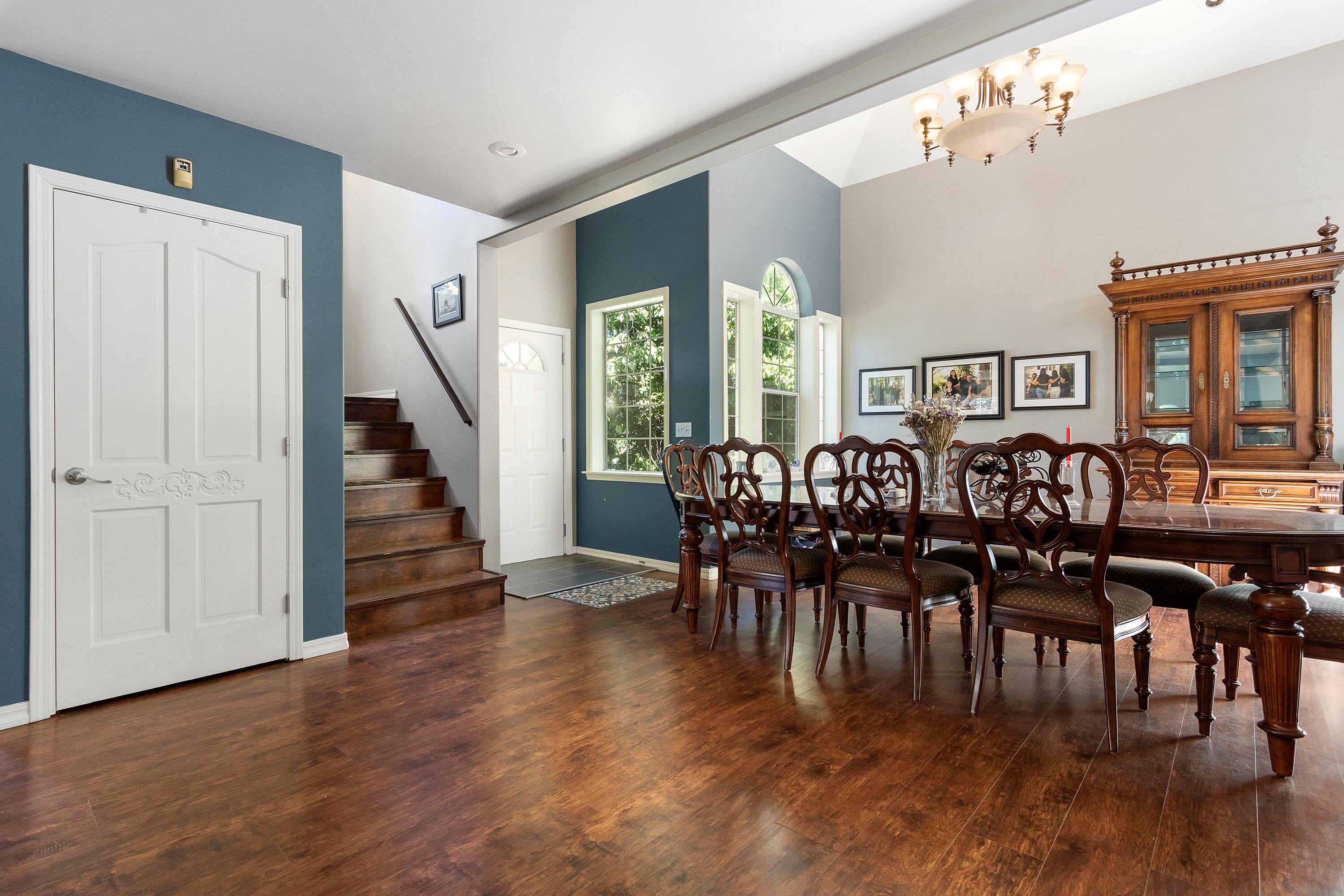 A dining area with a wooden table and chairs, a staircase, and a view of the outdoors.
