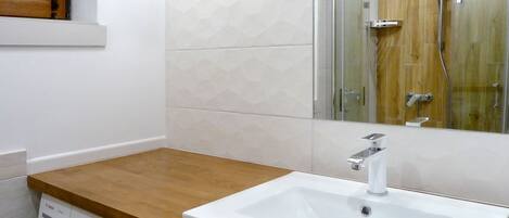 A bathroom with a wooden countertop, a white sink, a washing machine, and a glass shower enclosure.