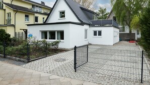 A modern two-story house with a white facade, a grey roof, and a fenced front yard.