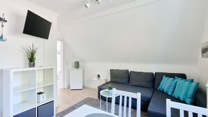 A modern living room with a grey sofa, white TV, and a small white table with a plant.