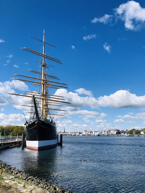 Un barco de gran altura amarrado en un puerto con cielo despejado y un pueblo lejano.