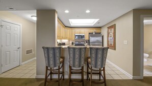 A kitchen with a central island, wooden cabinets, a microwave, oven, and refrigerator. There are three bar stools with patterned upholstery.