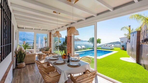 A dining area with a table set for four, overlooking a swimming pool and a lush green lawn.