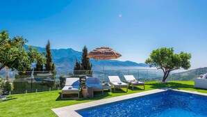 A poolside area with lounge chairs, a thatched umbrella, and a view of mountains.