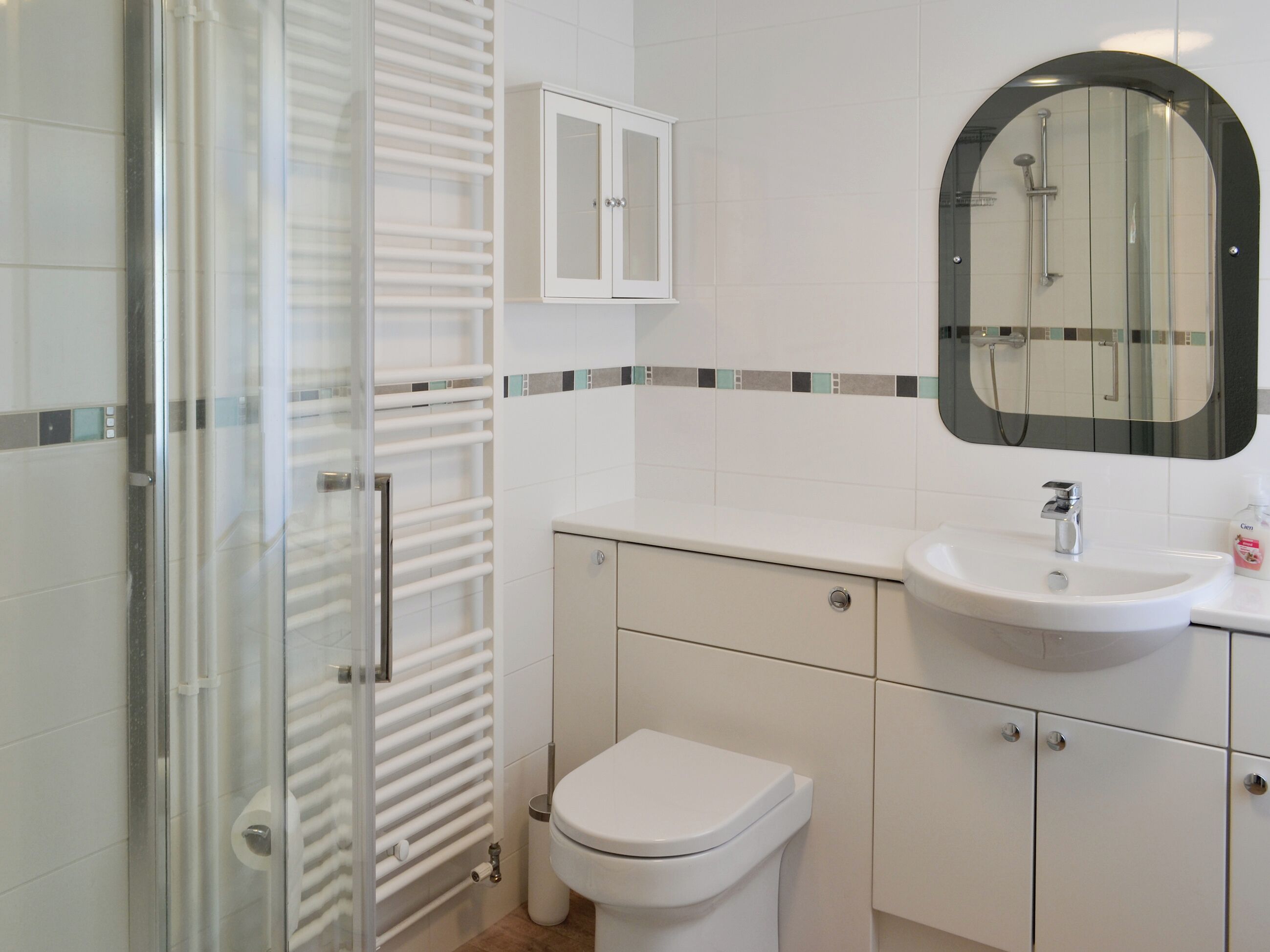 A modern bathroom with a glass shower enclosure, a white toilet, a sink with a mirror above it, and a cabinet with a tiled backsplash.