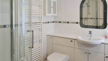 A modern bathroom with a glass shower enclosure, a white toilet, a sink with a mirror above it, and a cabinet with a tiled backsplash.