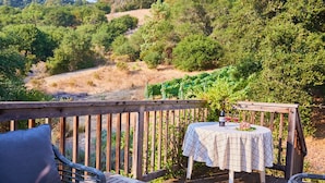 Una terraza de madera con mesa y sillas, con vista a un viñedo.