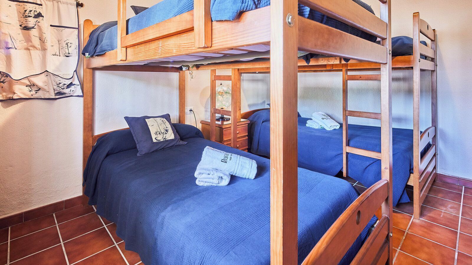 Une chambre avec un lit superposé, composé de deux lits, chacun doté d’un matelas et d’oreillers bleus. On y trouve une tête de lit en bois et une petite commode en bois avec un miroir.