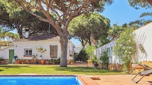 A poolside view of a house with a tiled roof, surrounded by potted plants and a large tree. - Villa Maymonis Chiclana de la Frontera by Ruralidays (Cádiz)