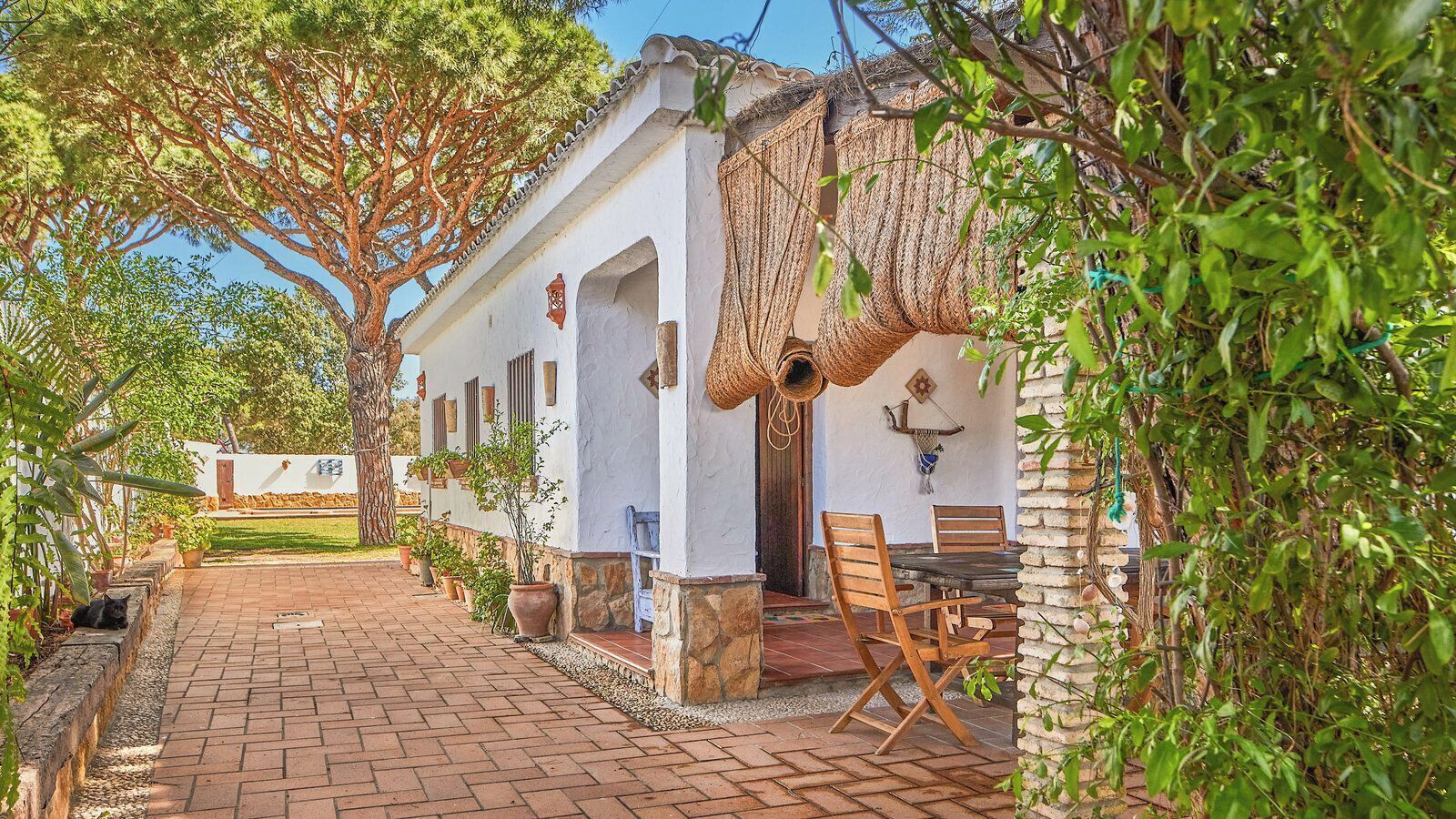 A white building with a tiled patio, wooden chairs, and a table.