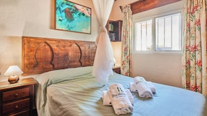 Een slaapkamer met een houten hoofdbord, een bed met een witte dekbedovertrek, een nachtkastje met een lamp, en twee handdoeken met een logo erop.