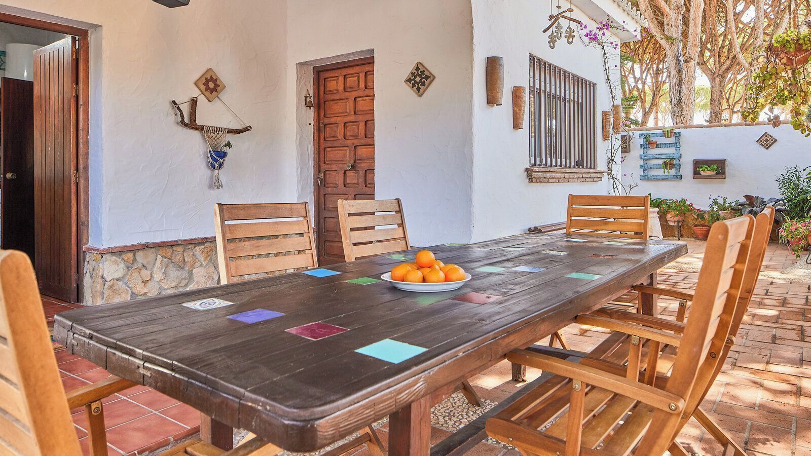 A wooden dining table with chairs, a plate of oranges, and decorative tiles on the floor.