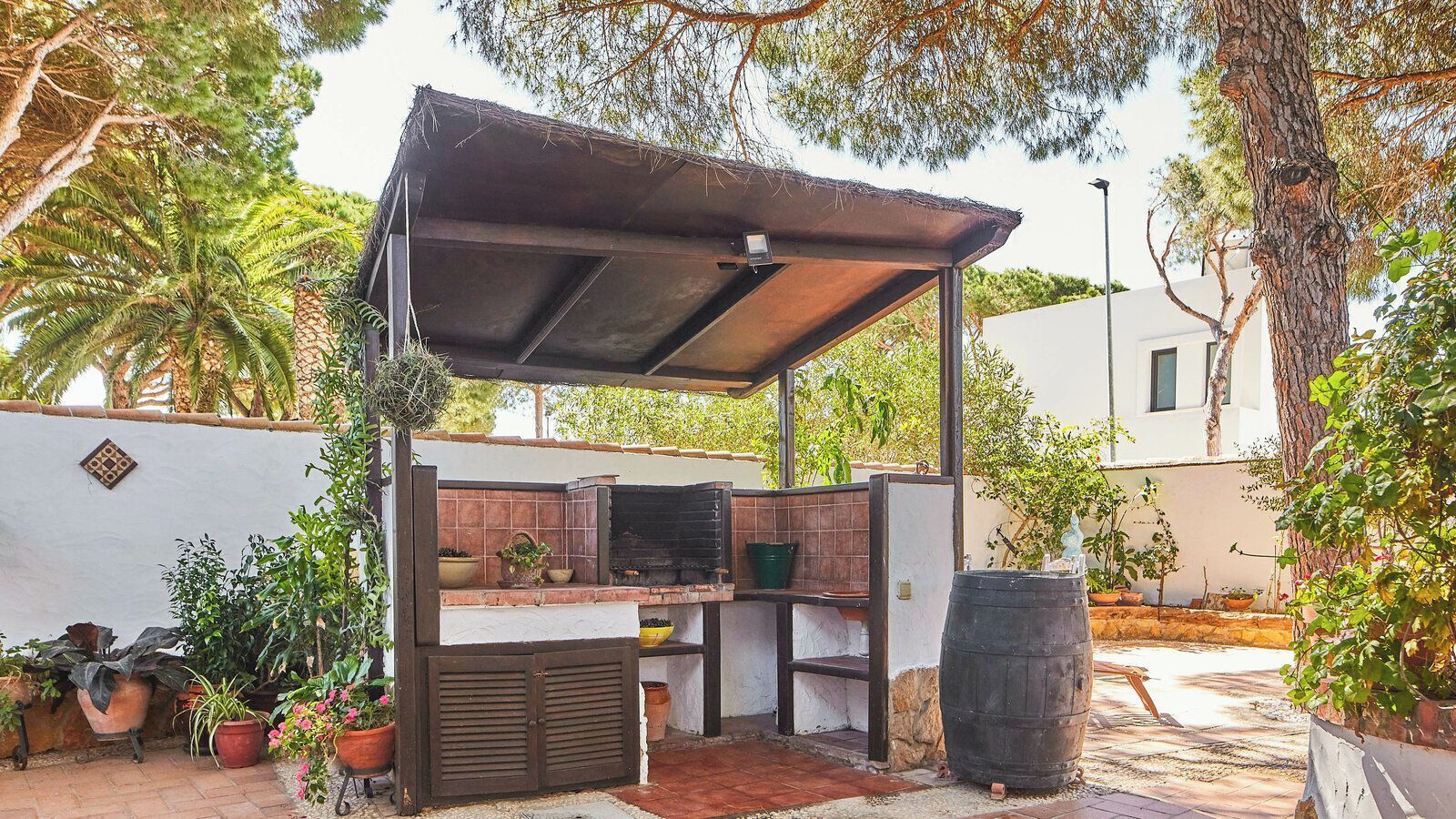 An outdoor kitchen with a metal roof, a brick oven, and potted plants.