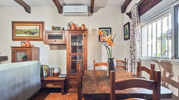 A cozy dining area with a wooden table and chairs, a cabinet with glass doors, a window with curtains, and a painting on the wall.