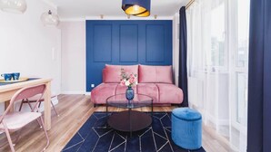 A modern living room with a blue sofa, a round coffee table, a pink chair, and a blue ottoman.