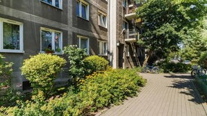 A multi-story residential building with balconies, a paved pathway, and lush greenery.