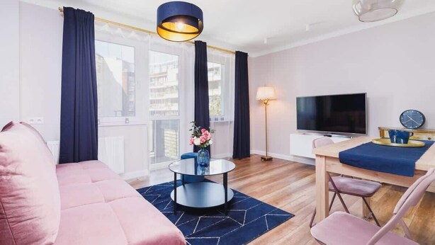 A modern living room with a sofa, a round coffee table, a TV, and a dining area with chairs and a table.