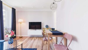 A modern living room with a flat-screen TV, a dining table with chairs, a lamp, and a vase of flowers.