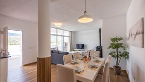 Un espace repas moderne avec une table blanche dressée pour quatre personnes, une grande fenêtre et une vue sur l’extérieur.