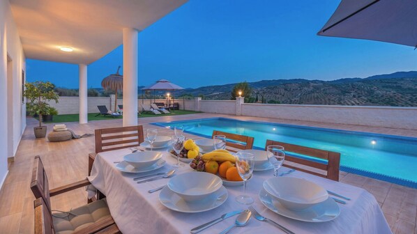 An outdoor dining area with a pool, tables set with white tablecloths, and a view of the mountains.