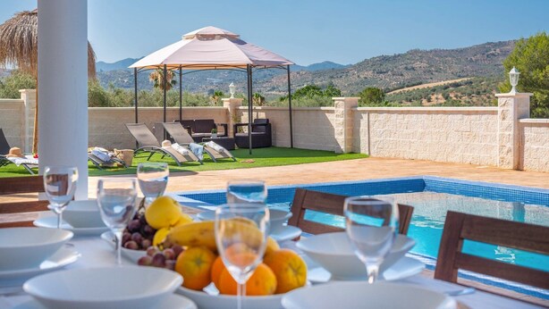 Un espace repas aménagé au bord de la piscine, avec une table pour deux, une piscine, des chaises longues et une pergola.