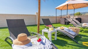 Une terrasse sur le toit avec deux chaises longues, une table sur laquelle se trouvent une pastèque, des boissons et un panier.