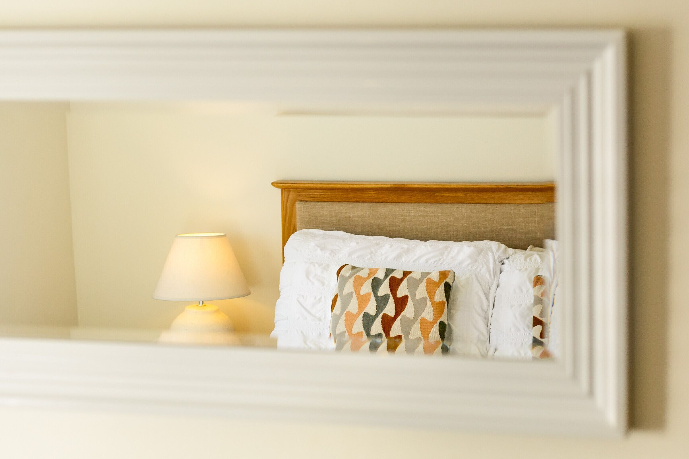 A neatly made bed with a patterned pillow and a bedside lamp.