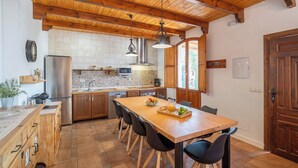 Een keuken met houten kastjes, een roestvrijstalen koelkast, een magnetron en een eettafel met stoelen.
