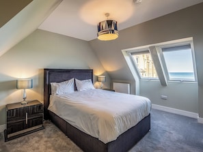 A bedroom with a bed, two bedside lamps, a dresser, a radiator, and a window with a view.