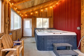 A wooden cabin interior with a hot tub, a door, and a chair.