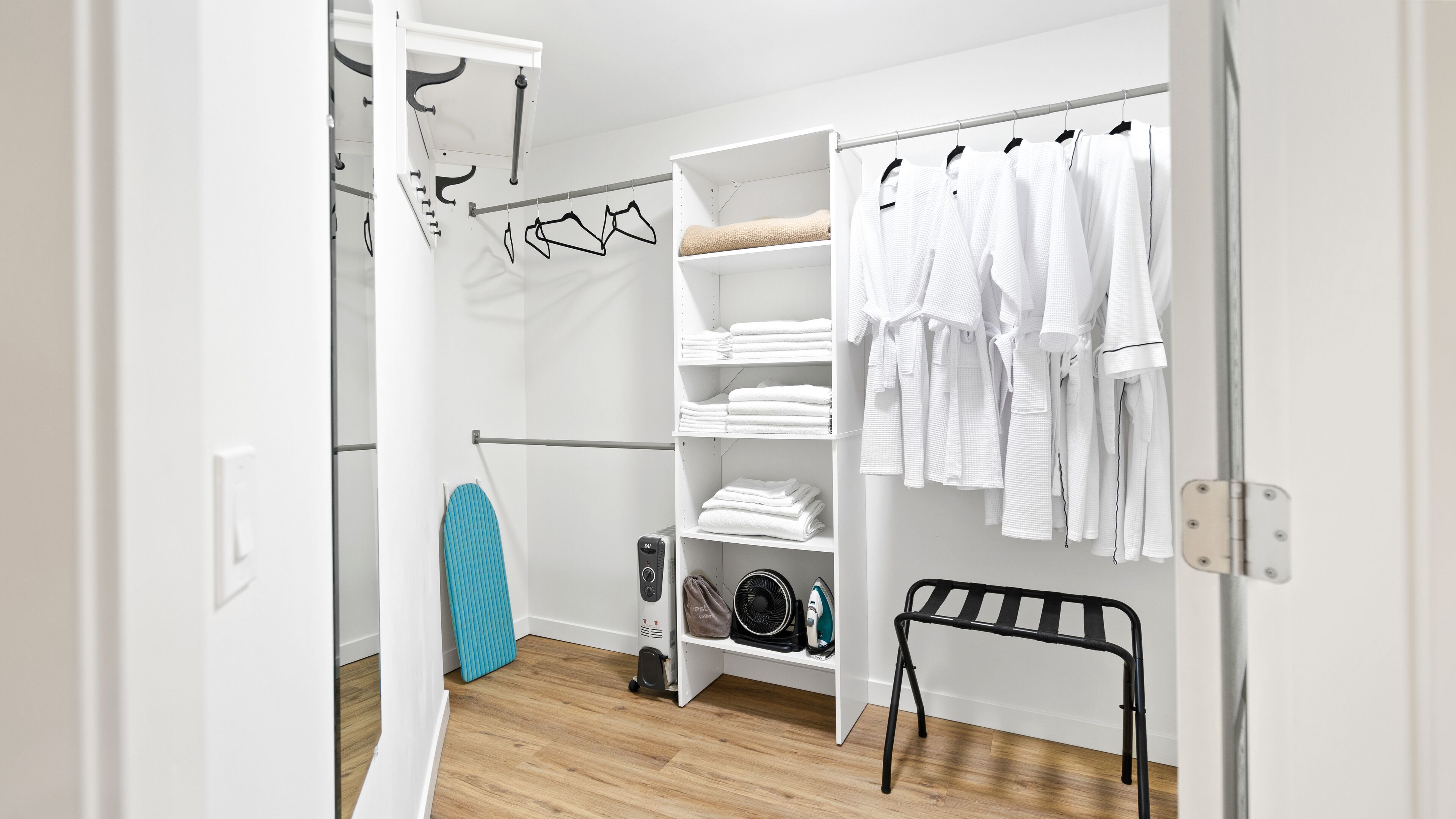 Ein begehbarer Kleiderschrank mit Regalen für gefaltete Kleidung, einem Wäscheständer und einem schwarzen Metallstuhl.