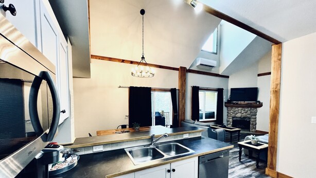 A modern kitchen with a built-in dishwasher, a large island with a sink, and a dining area with a stone fireplace.