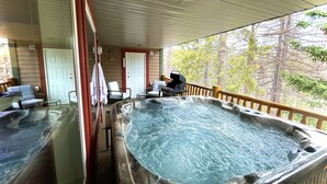 A covered outdoor area with two hot tubs, wooden deck, chairs, and a door.