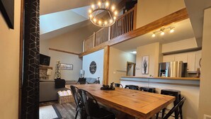 A dining area with a wooden table and chairs, a chandelier, and a staircase leading to an upper level.