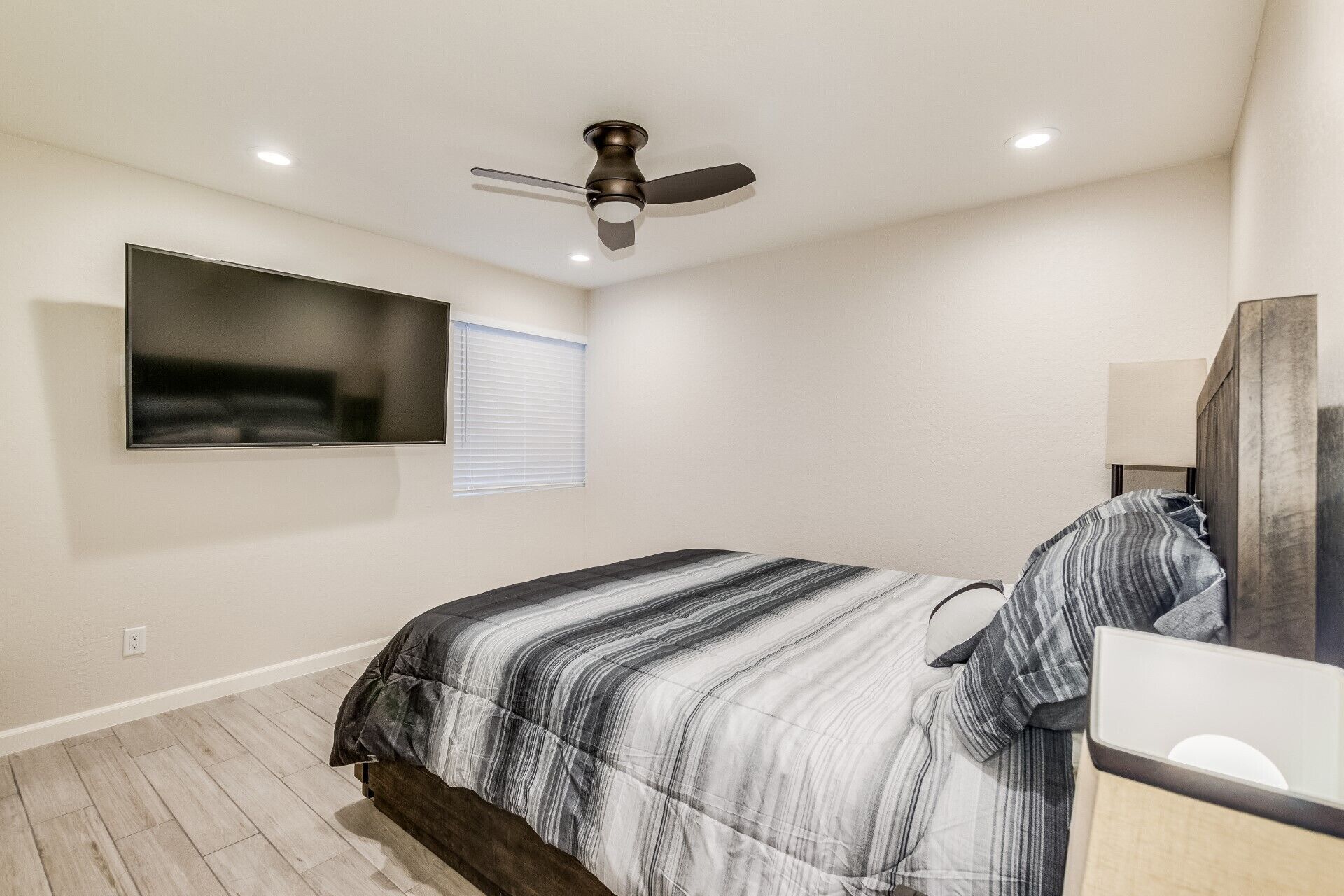 A bedroom with a bed, a ceiling fan, a TV mounted on the wall, and a bedside table.