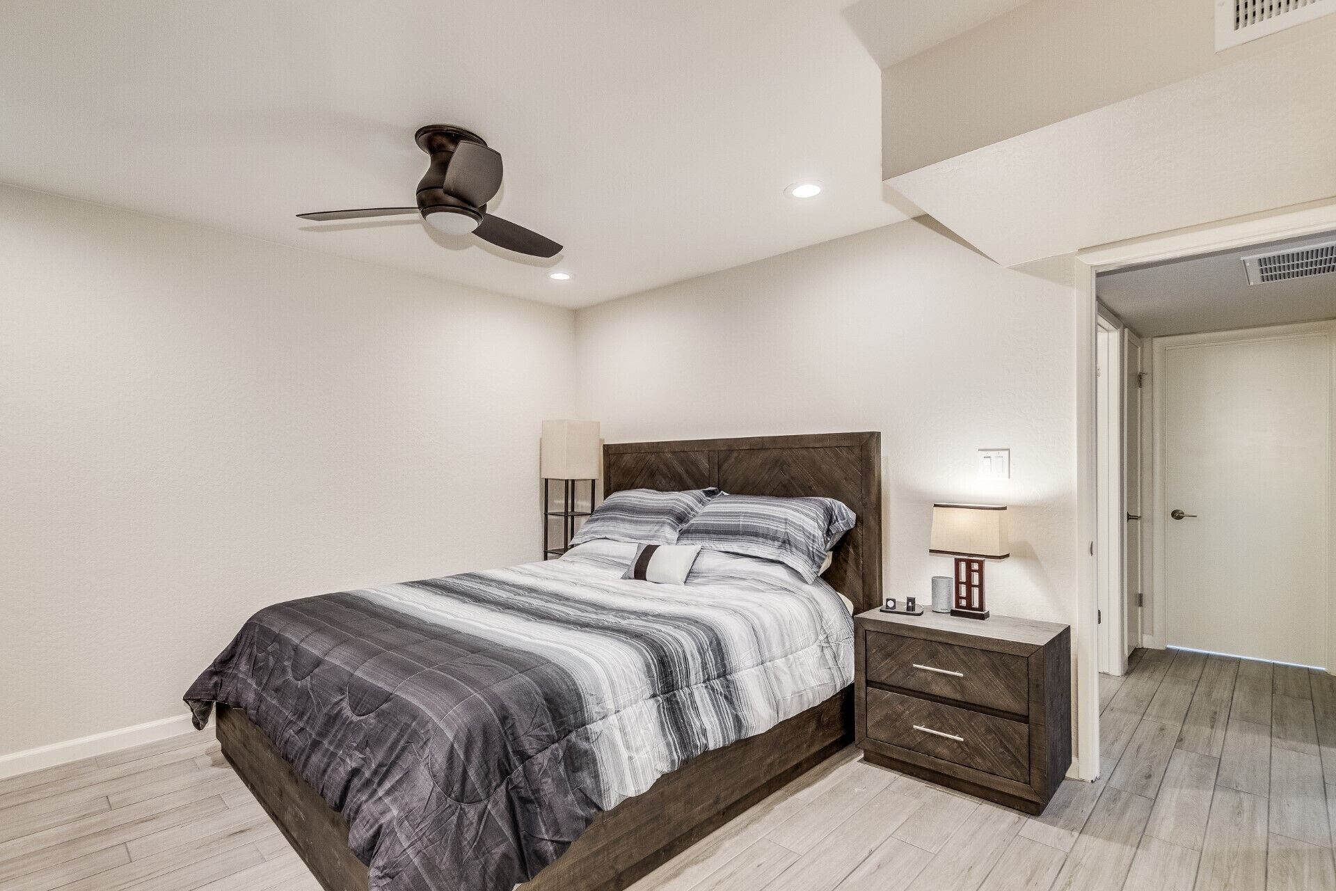 Quarto com cama, mesas de cabeceira, ventilador de teto e porta para outro cômodo.