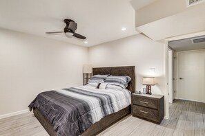 Quarto com cama, mesas de cabeceira, ventilador de teto e porta para outro cômodo.